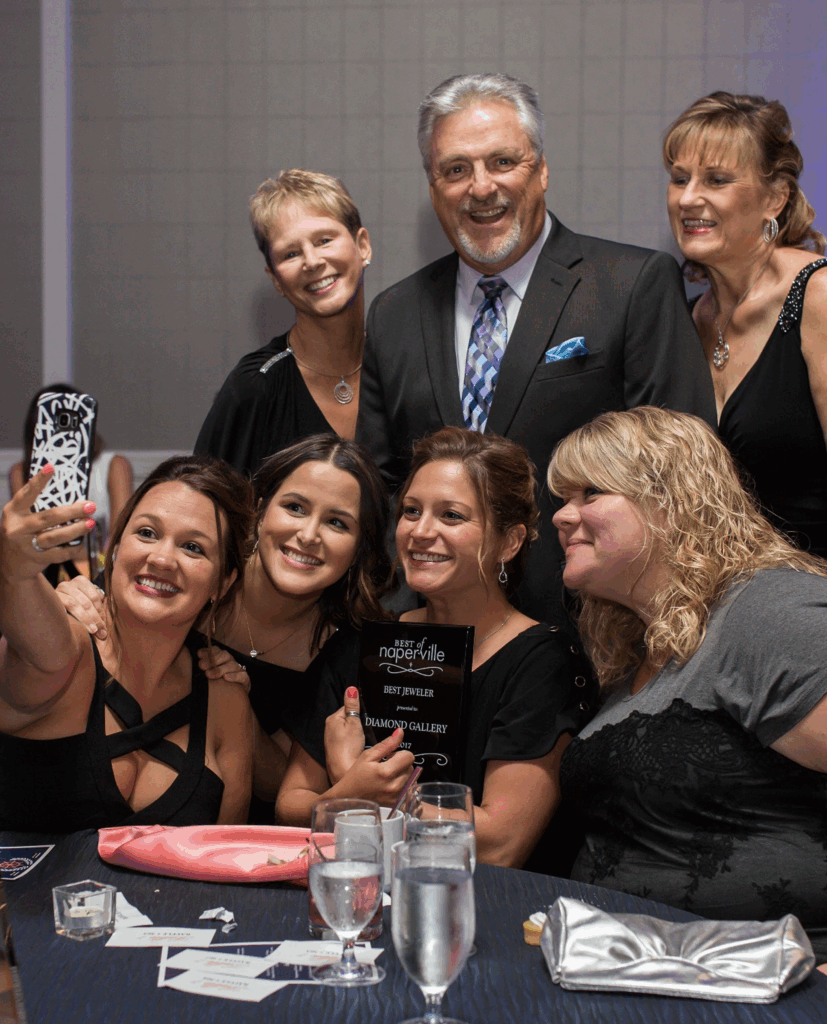 Six women smiling and posing for a selfie at an event, two holding awards.